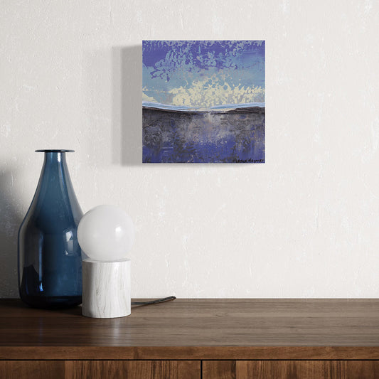 Blue,abstract painting on a wall above a wooden surface with a blue vase and white lamp.