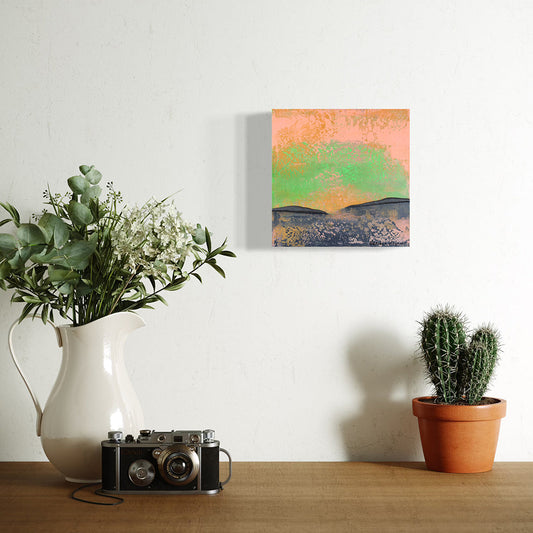 Heather Haymart original painting on the wall with decorative setting with a pitcher of flowers, vintage camera, and potted cactus on a wooden surface.