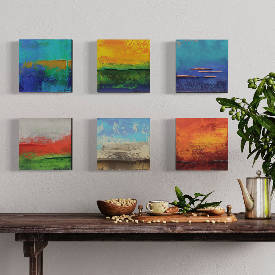 Set of six colorful abstract paintings on a wall above a wooden table with decorative items.