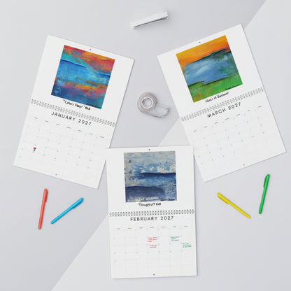Three printed monthly calendar pages laid out on a light gray surface with art prints for January, March, and February 2027. The pages feature colorful abstract landscape paintings at the top and are styled with tape and pens around them.