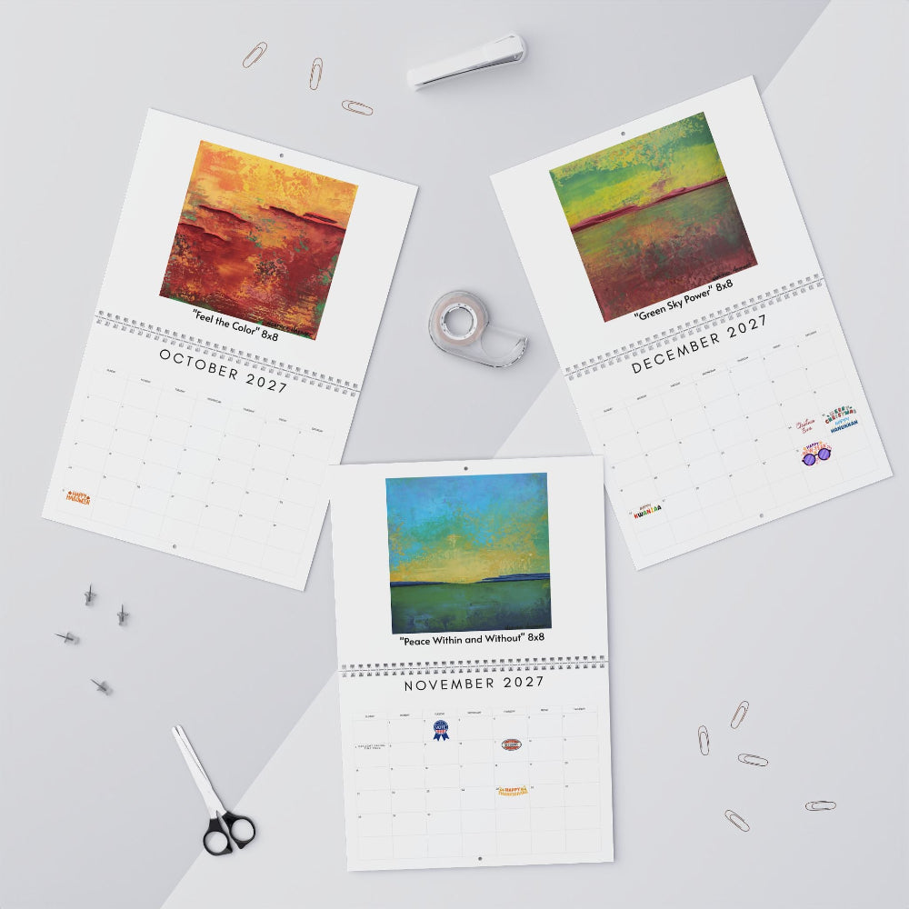 Three printed monthly calendar pages laid out on a light gray surface, each featuring a colorful landscape artwork and the titles with October, December, and November 2027 dates visible.