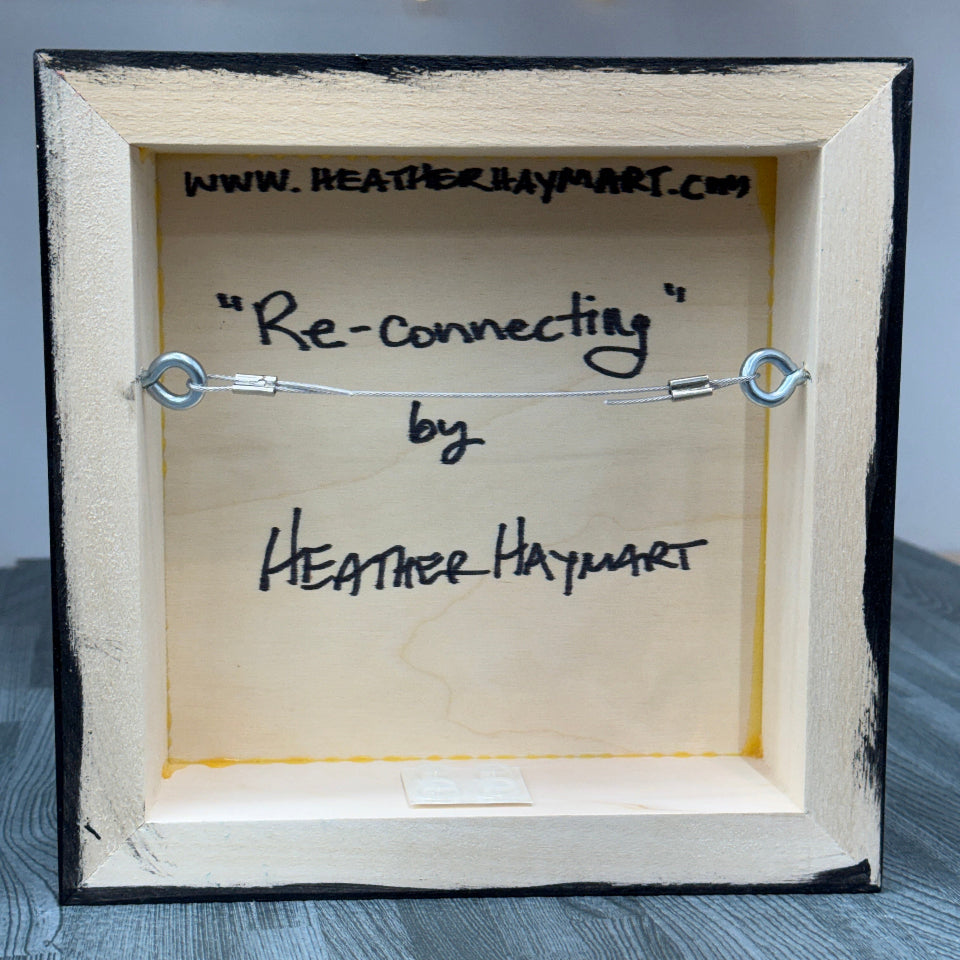 Wooden box with a hanging wire labeled 'Re-connecting' by Heather Haymart on a gray surface.