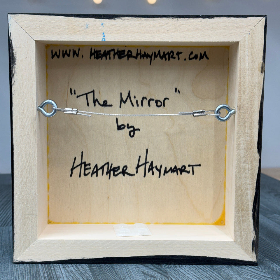 Wired, wooden frame with 'The Mirror' by Heather Haymart text on a gray background