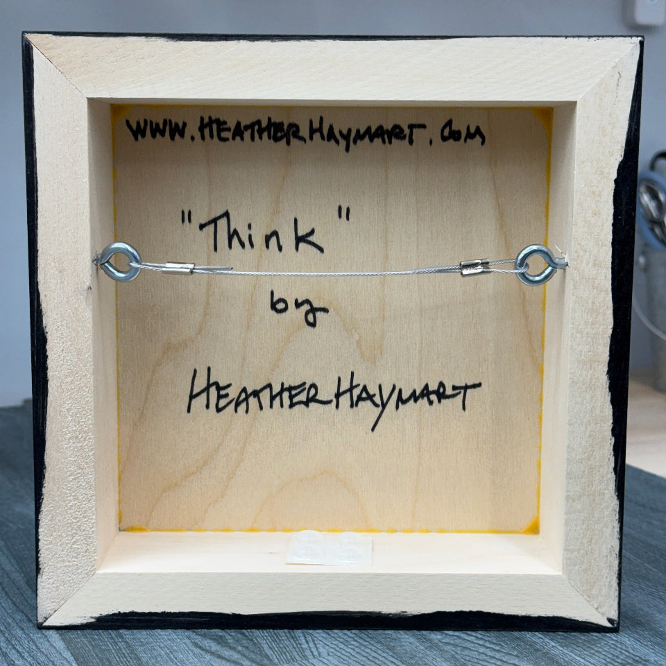 Wooden box with wire, signed 'Think' by Heather Haymart on a gray surface.