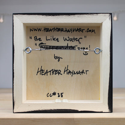 Framed artwork with text and a metal hook on a neutral background