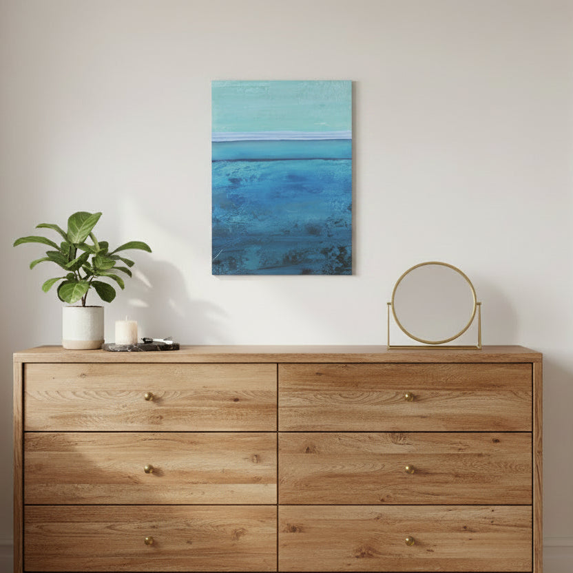 Abstract blue canvas art print on a white wall above a dresser with decor items.
