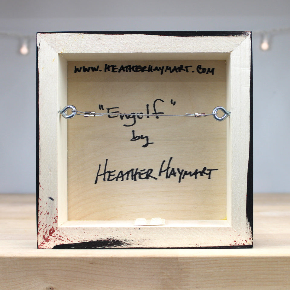 Framed artwork with a string and hook, signed by Heather Haymart, on a light background.