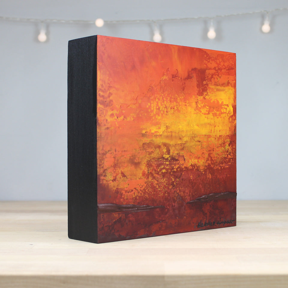 Abstract art piece with orange and red hues on a black frame, displayed indoors.