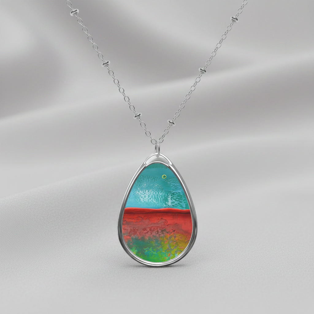 A teardrop-shaped art pendant necklace with a colorful abstract design, featuring a brass pendant on a silver chain.