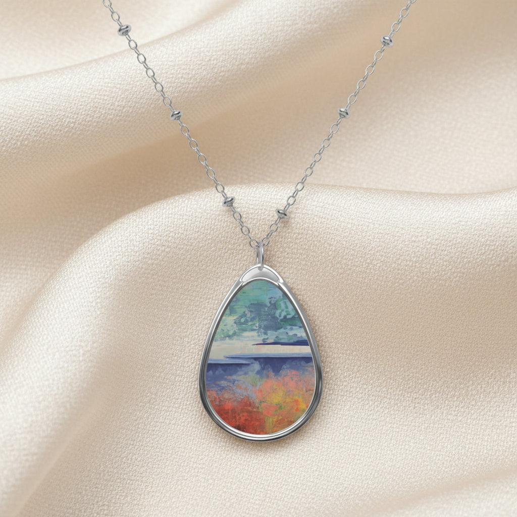 A teardrop-shaped art pendant necklace with a white aluminum print surface featuring a colorful painting, suspended from a silver chain.