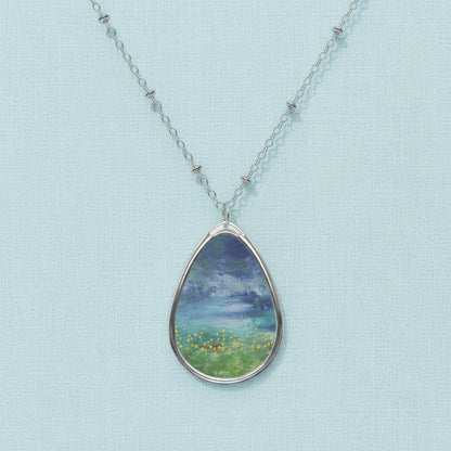 A teardrop-shaped art pendant necklace with a white and blue color scheme, featuring an artistic depiction of a natural scene.