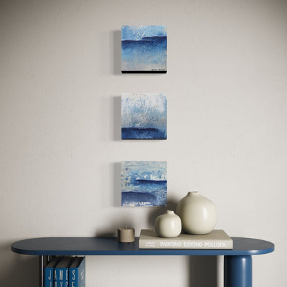 Three abstract blue paintings arranged vertically on a wall above a table with decorative items.