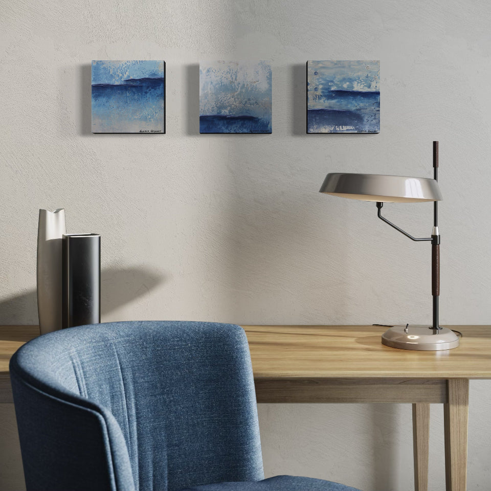 Three art pieces hanging over modern office setup with a desk, chair, lamp, and wall art.