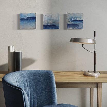 Three art pieces hanging over modern office setup with a desk, chair, lamp, and wall art.